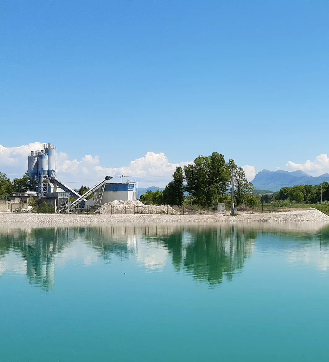 Plan d’eau artificiel turquoise au pied des montagnes de la Drôme, avec en arrière-plan une installation industrielle liée à l’extraction de granulats.